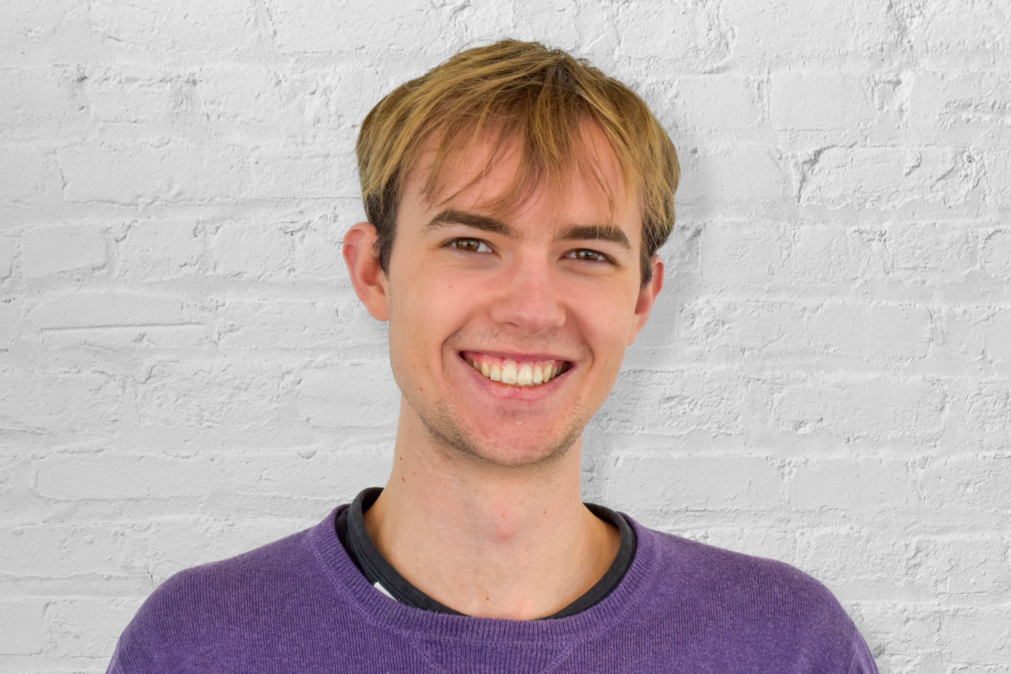 a person smiling in front of a brick wall