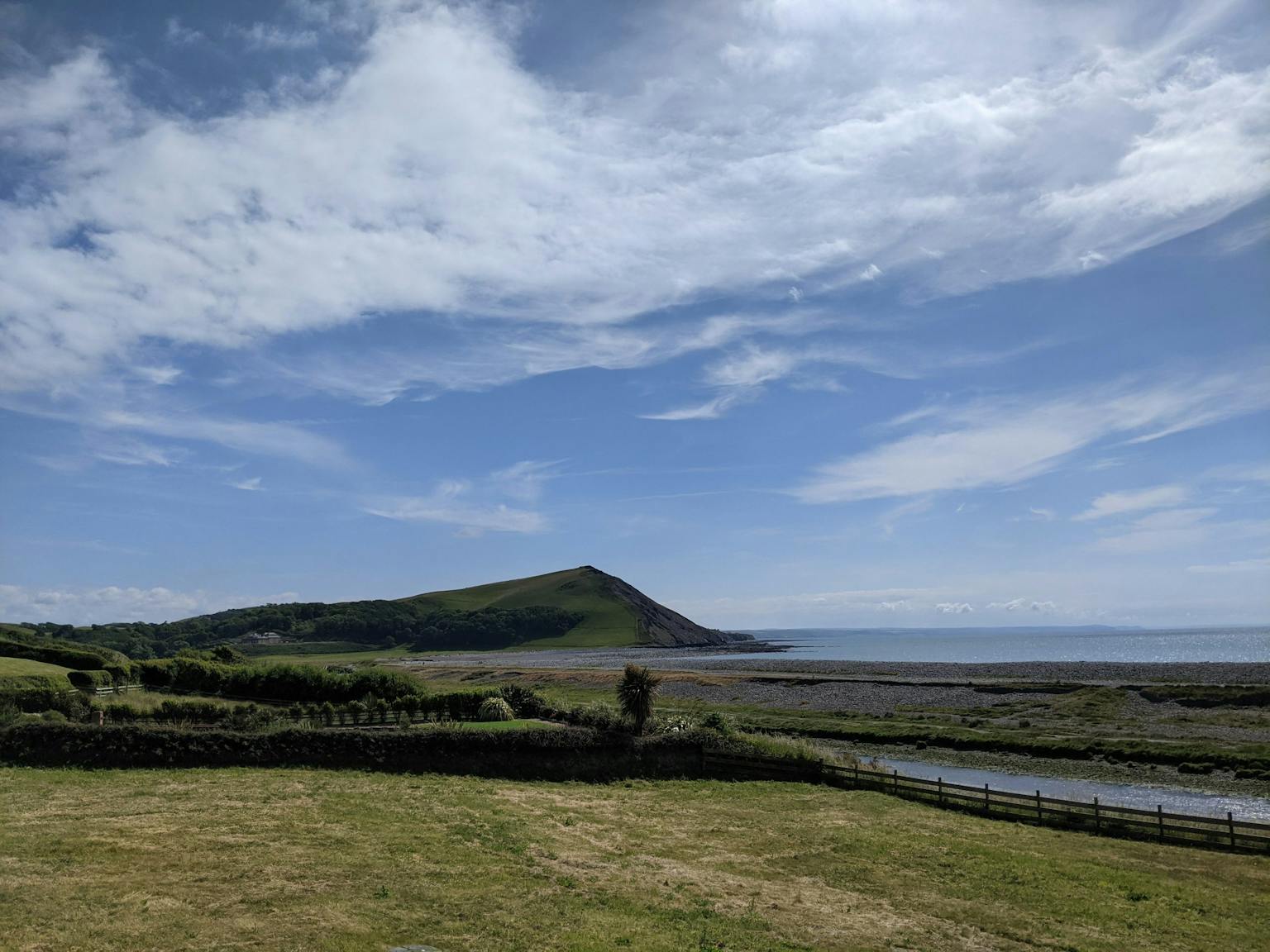 a grassy field with a body of water and a hill in the background