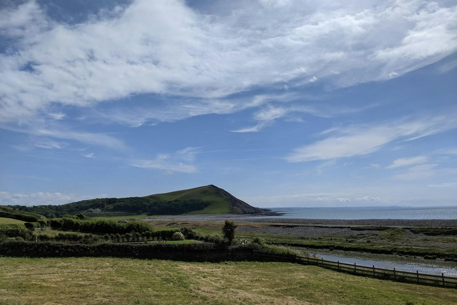 a grassy field with a body of water and a hill in the background