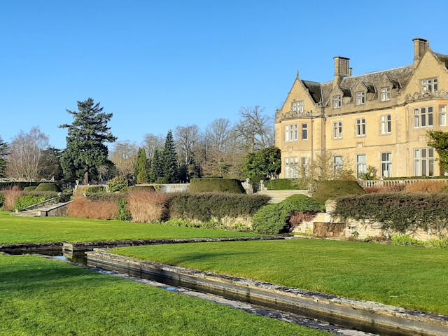 a large lawn with a stream in the middle and a country house in the background