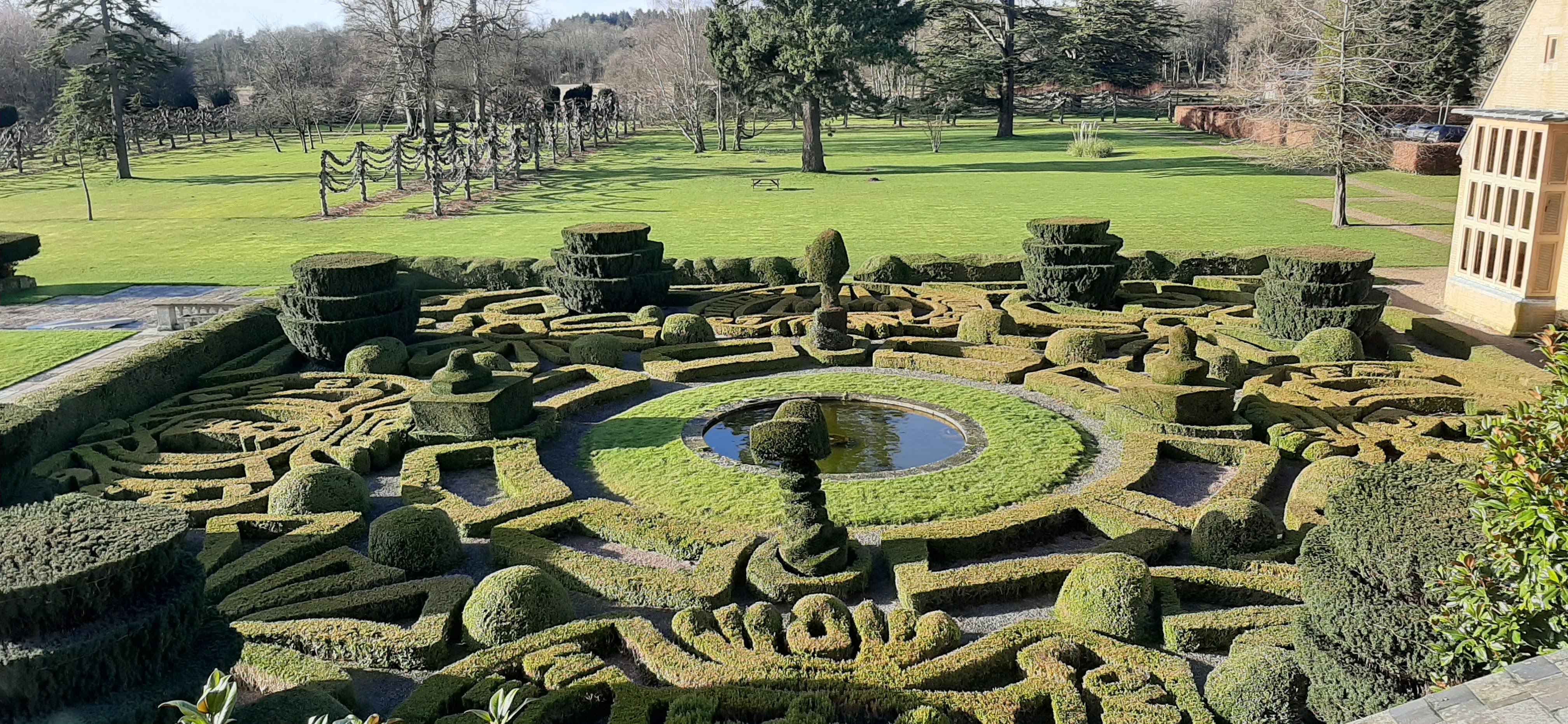 a garden with a maze, pond and trees