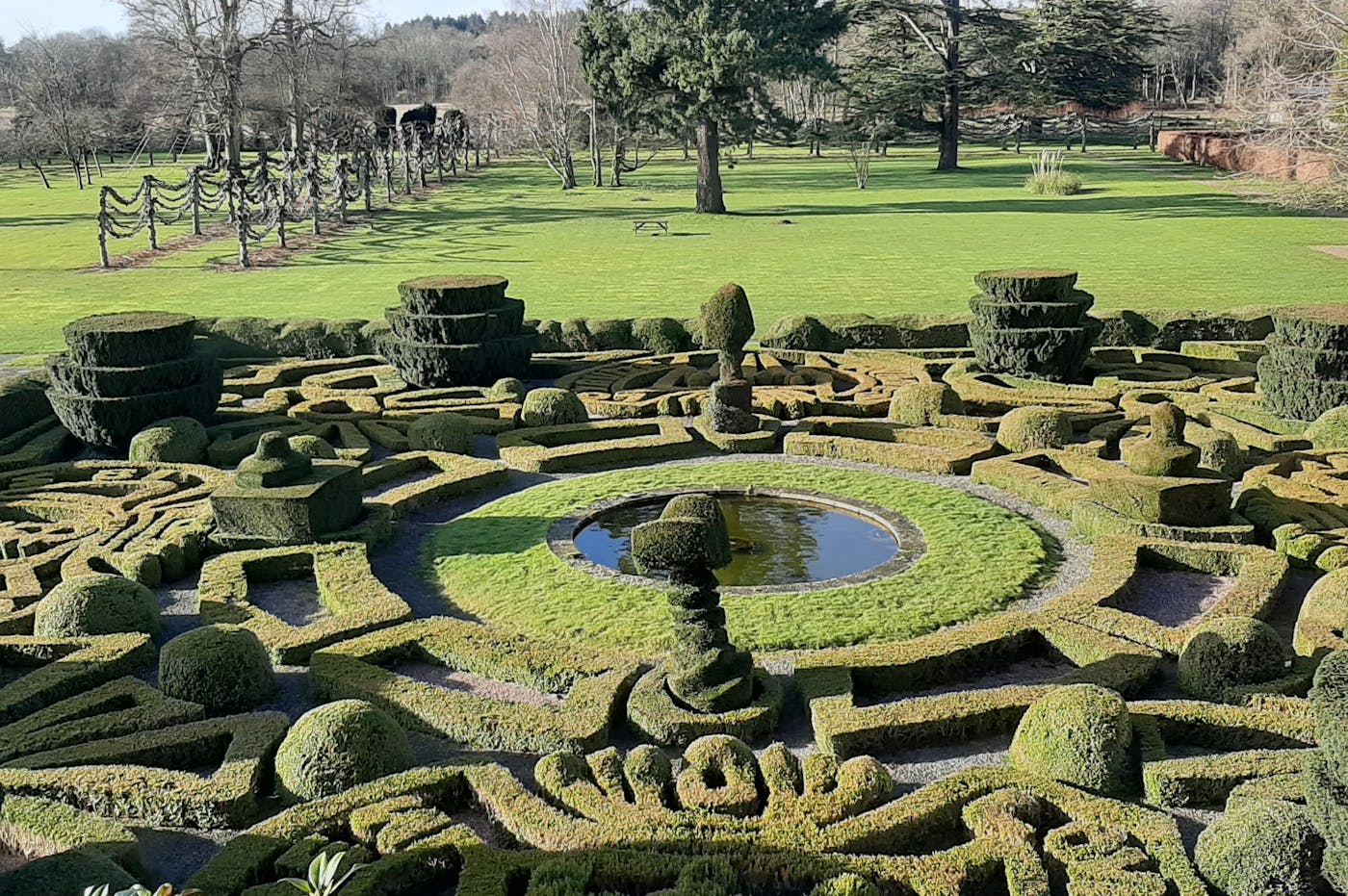 a garden with a maze, pond and trees