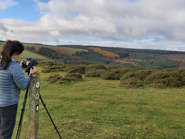 Countryside and hills. A person in the foreground with a camera on a tripod