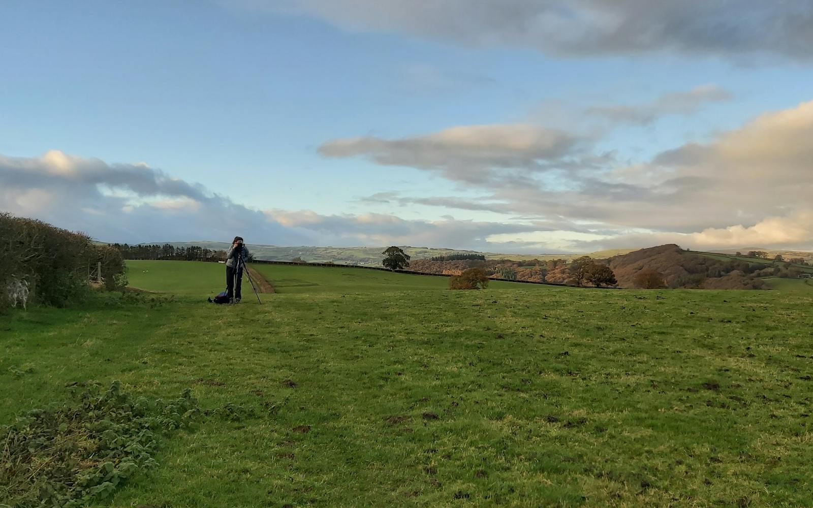 Countryside and hills. A woman with a camera on a tripod in the middle distance