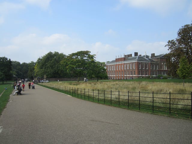A palace building surrounded by grassland and a road with people walking by