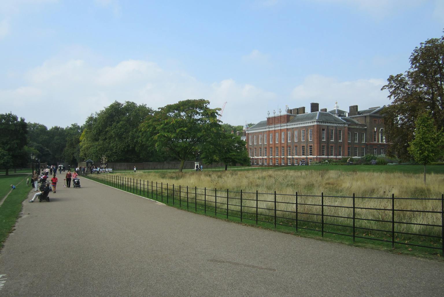 A palace building surrounded by grassland and a road with people walking by