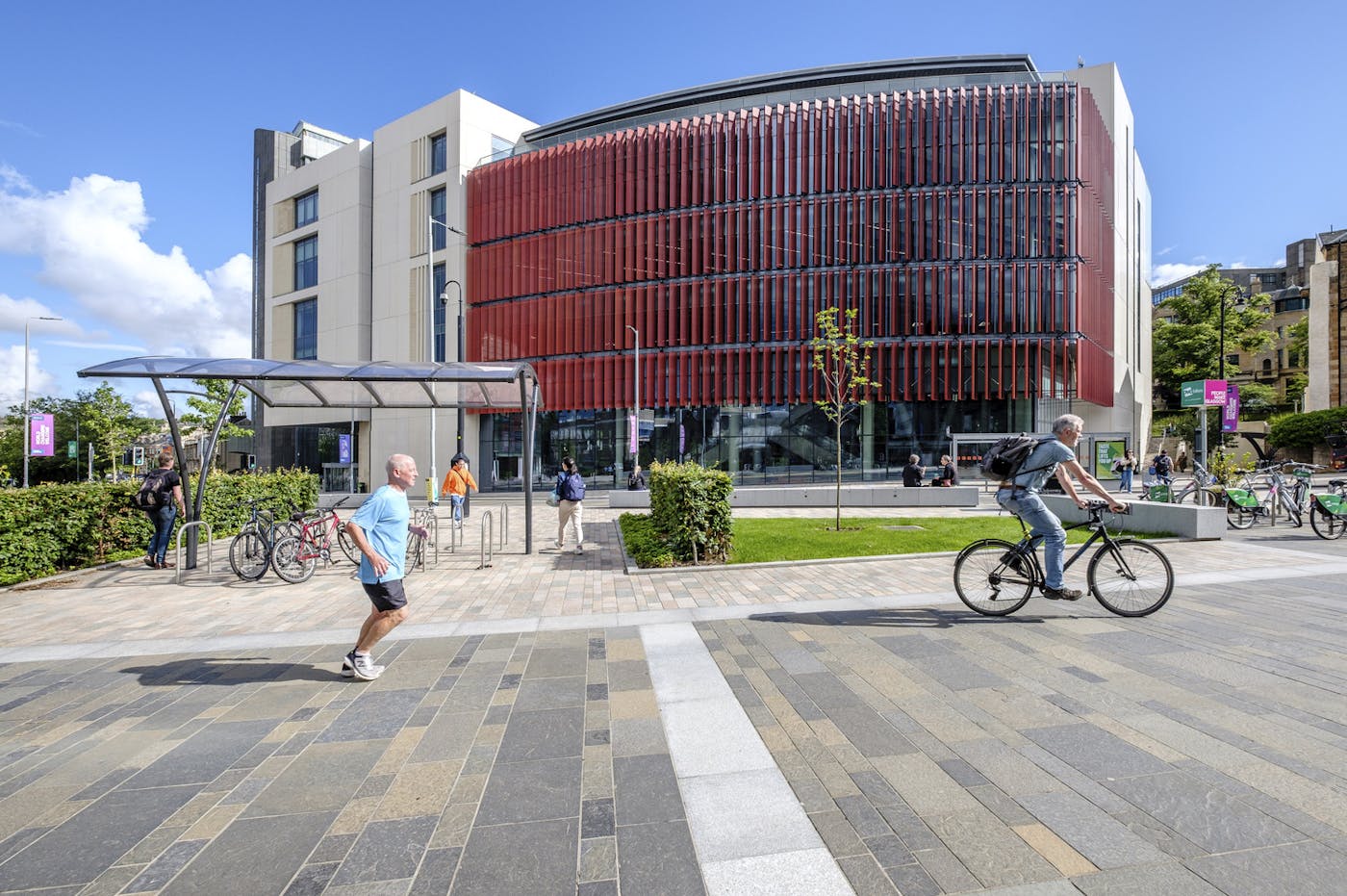 People walking and cycling in front of pavement in front of university building