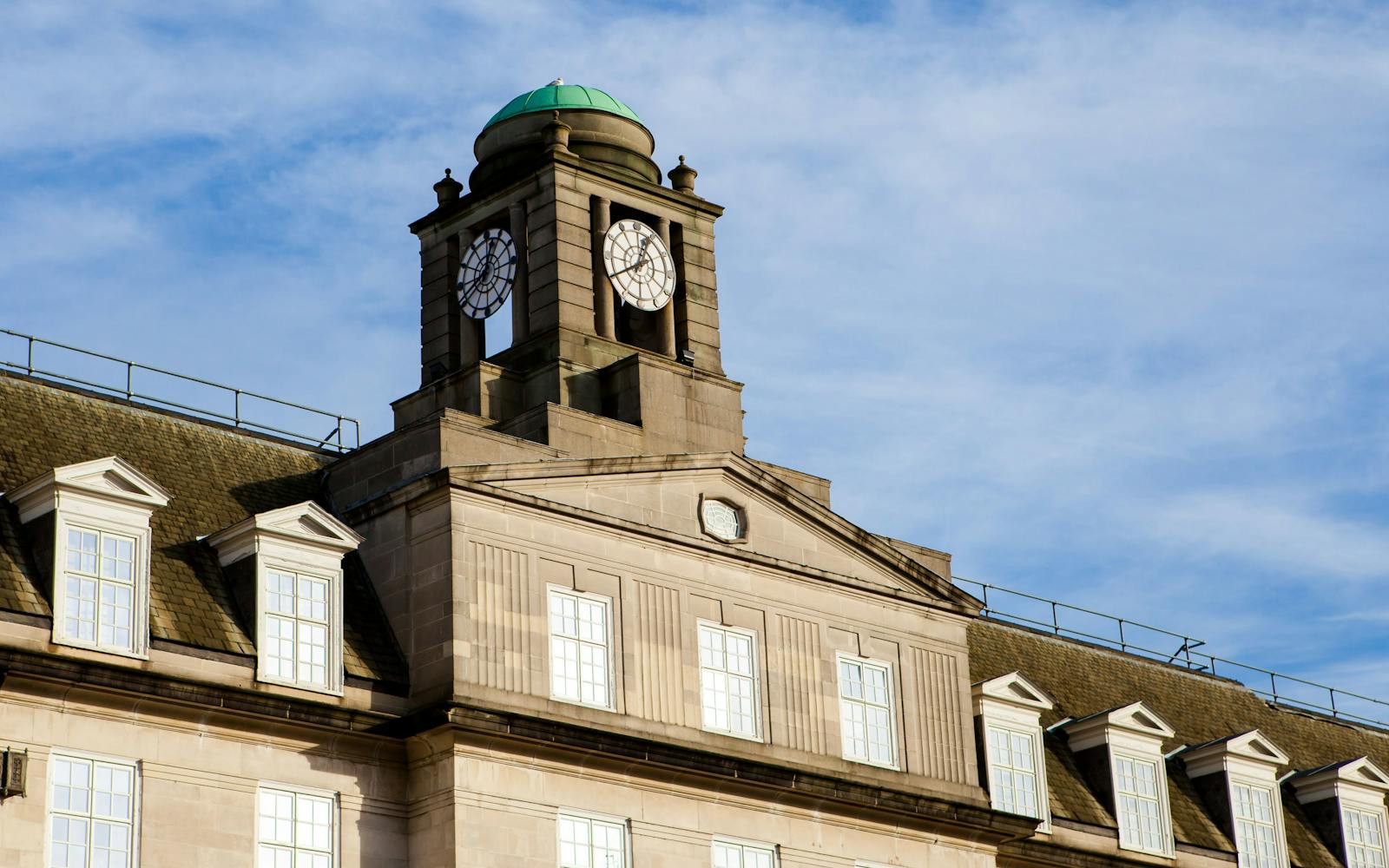 a historic clock tower hotel with a mansard roof and many windows, under a clear blue sky