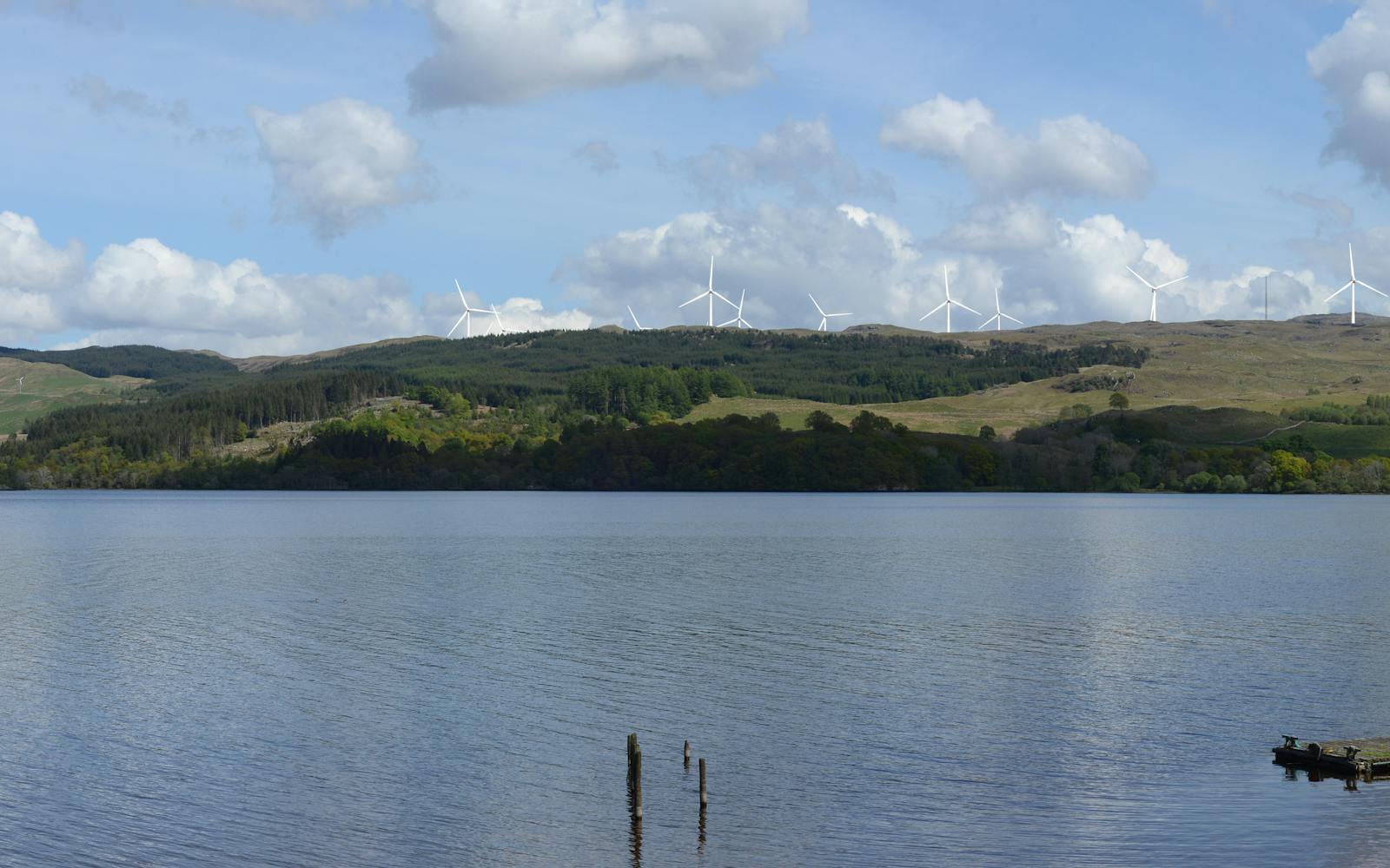 A loch with boats and hills with wind turbines in the background
