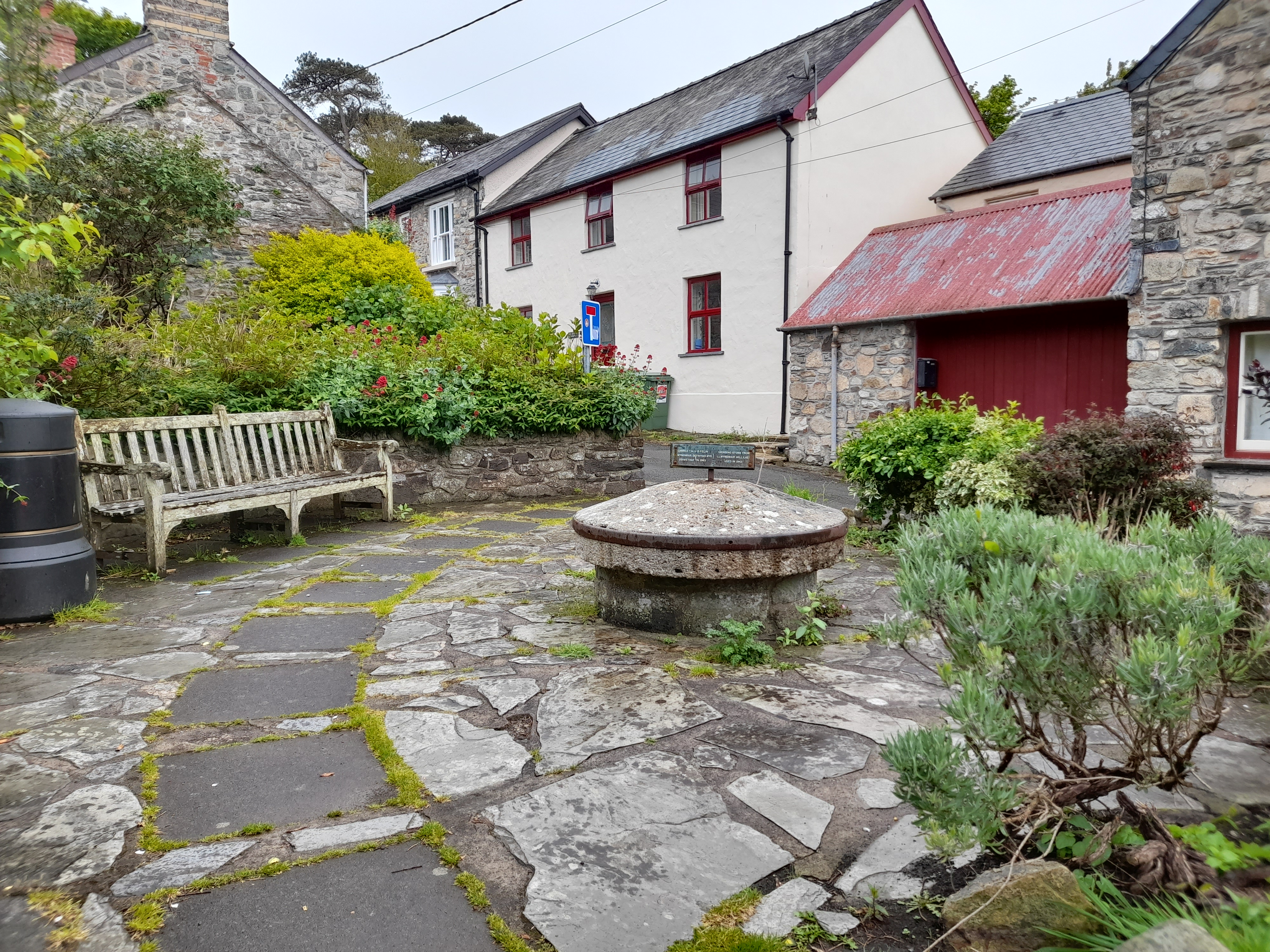 Stone patio with a bench and a well in front of a white house