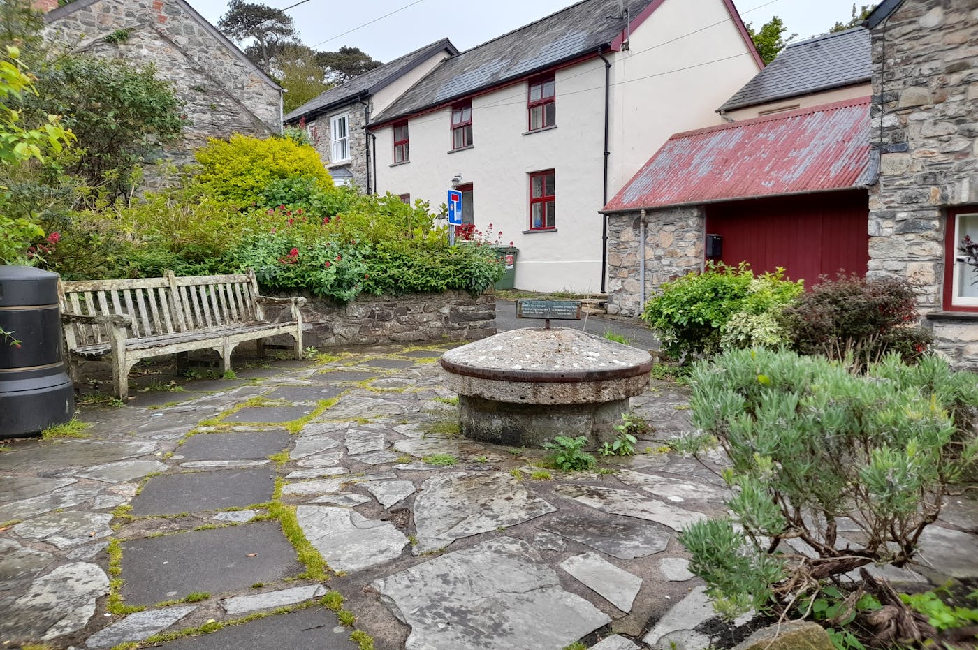 Stone patio with a bench and a well in front of a white house