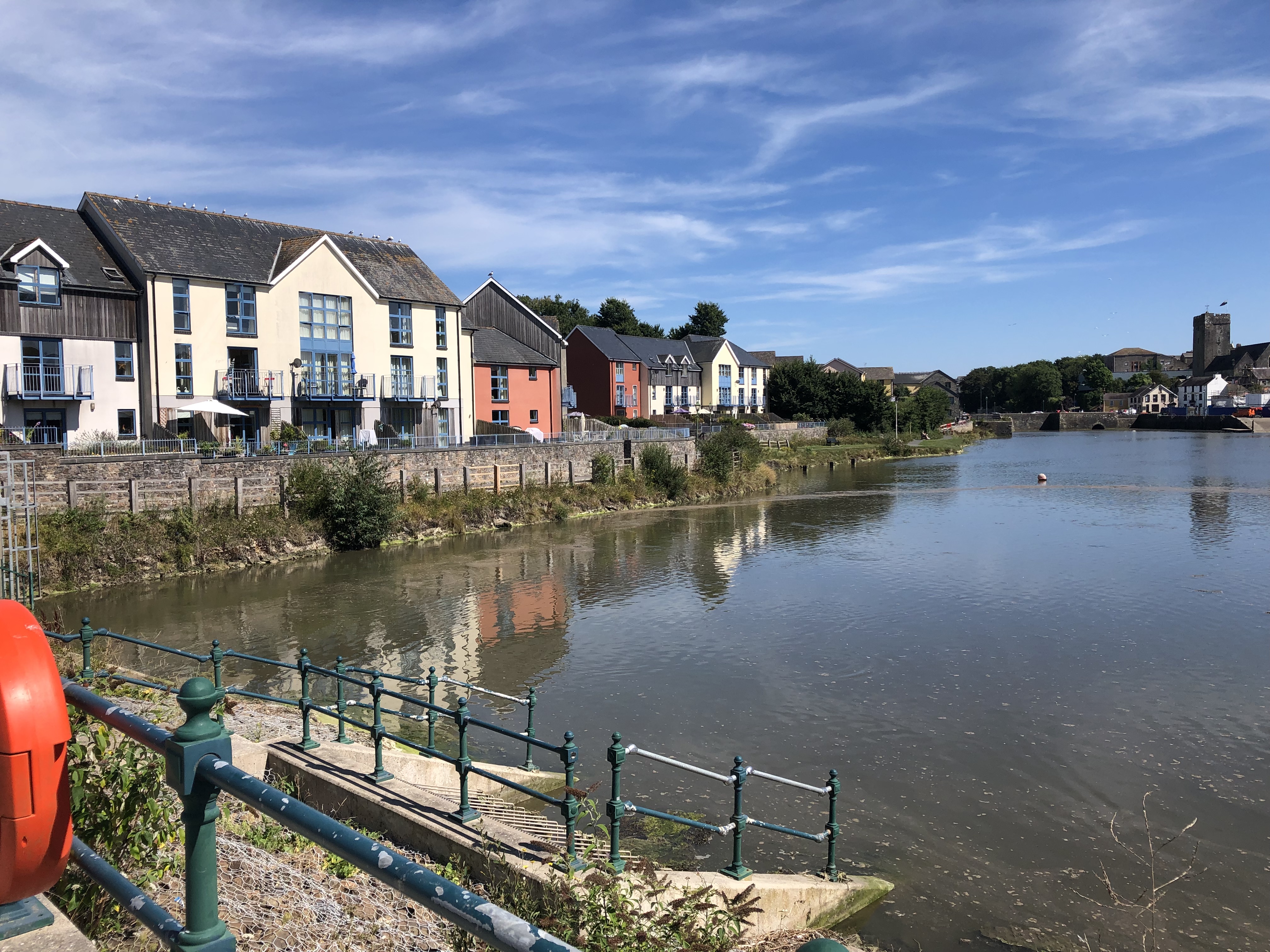 A row of colourful houses lining a riverbank, with a fence and life preserver in the foreground