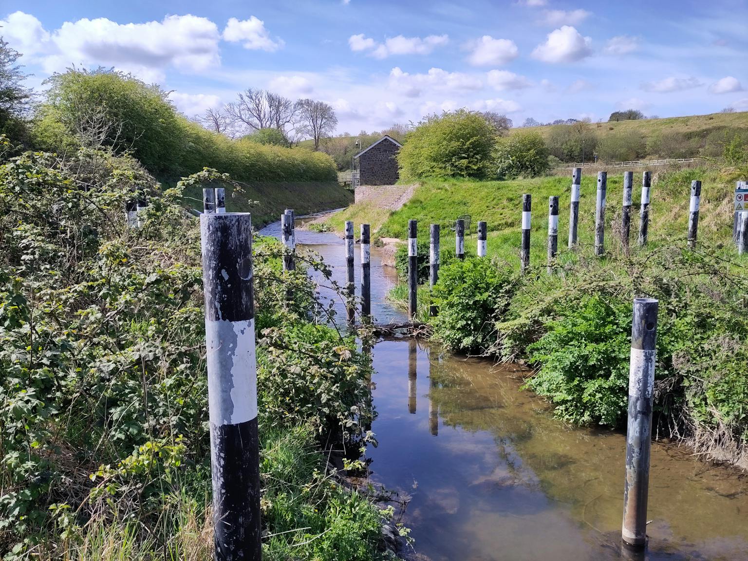 A clear stream with black and white painted poles lining its banks