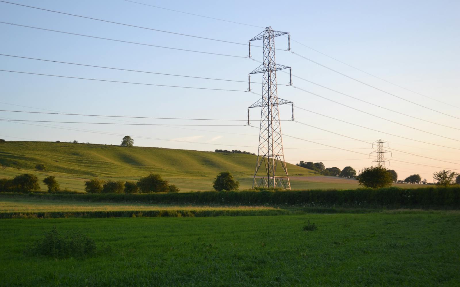 A high-voltage electricity pylon silhouetted against a colorful sunset in a rural field