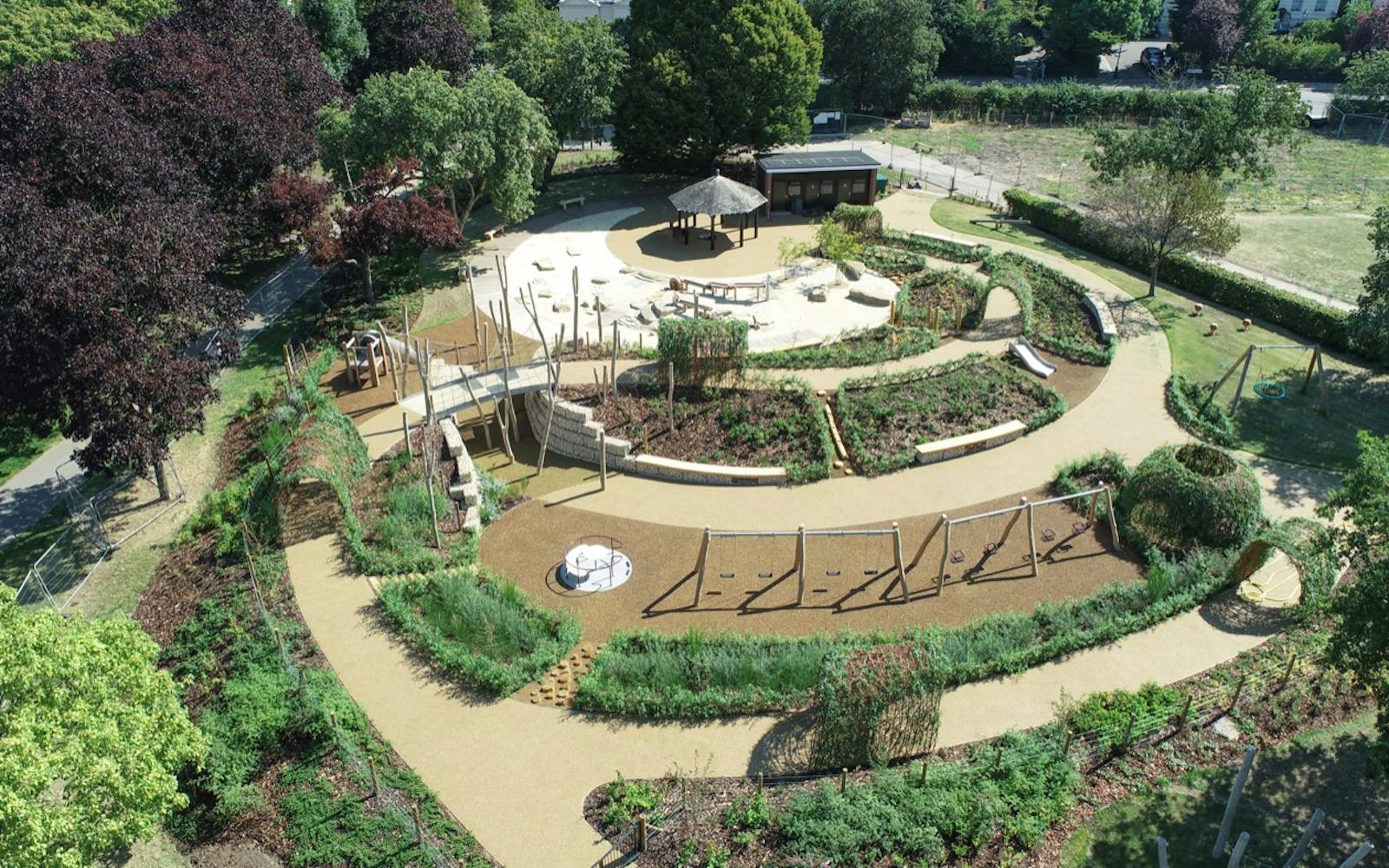 Playground equipment in a park with grassy field | Children playing. Aerial view of a park playground with slides, swings, climbing frames, and a sandpit, with children playing and enjoying the equipment