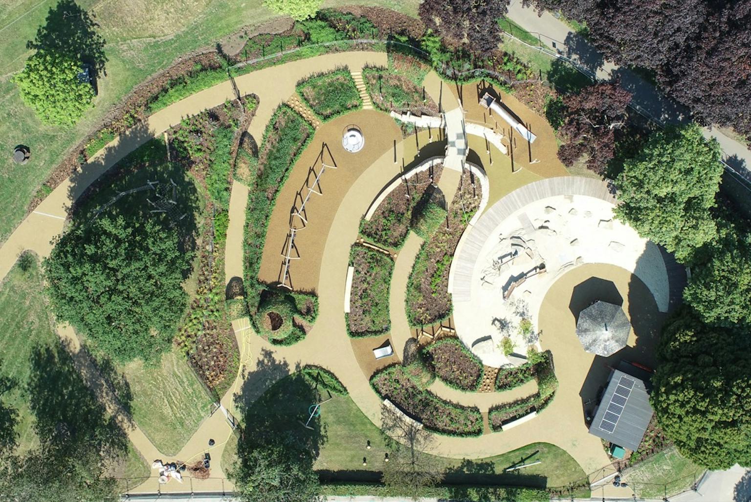 Playground equipment in a park with grassy field | Children playing. Aerial view of a park playground with slides, swings, climbing frames, and a sandpit, with children playing and enjoying the equipment