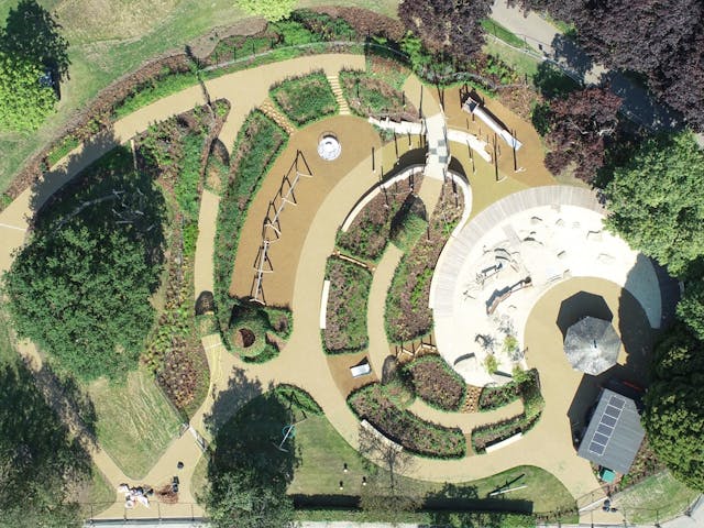 Playground equipment in a park with grassy field | Children playing. Aerial view of a park playground with slides, swings, climbing frames, and a sandpit, with children playing and enjoying the equipment