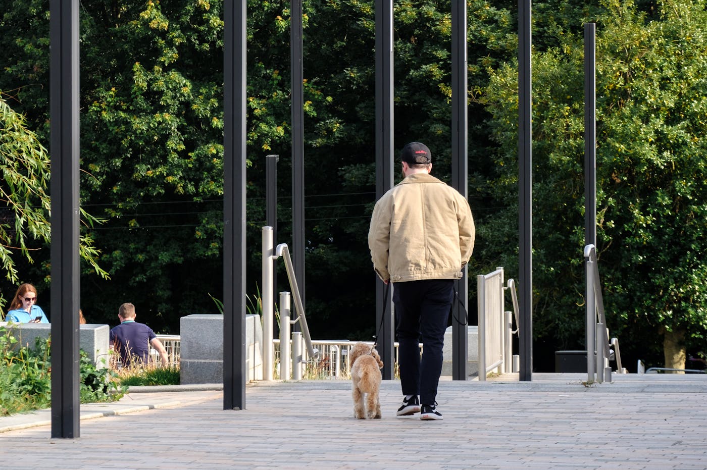 a man walking down a walkway with tall poles and a tower in the background