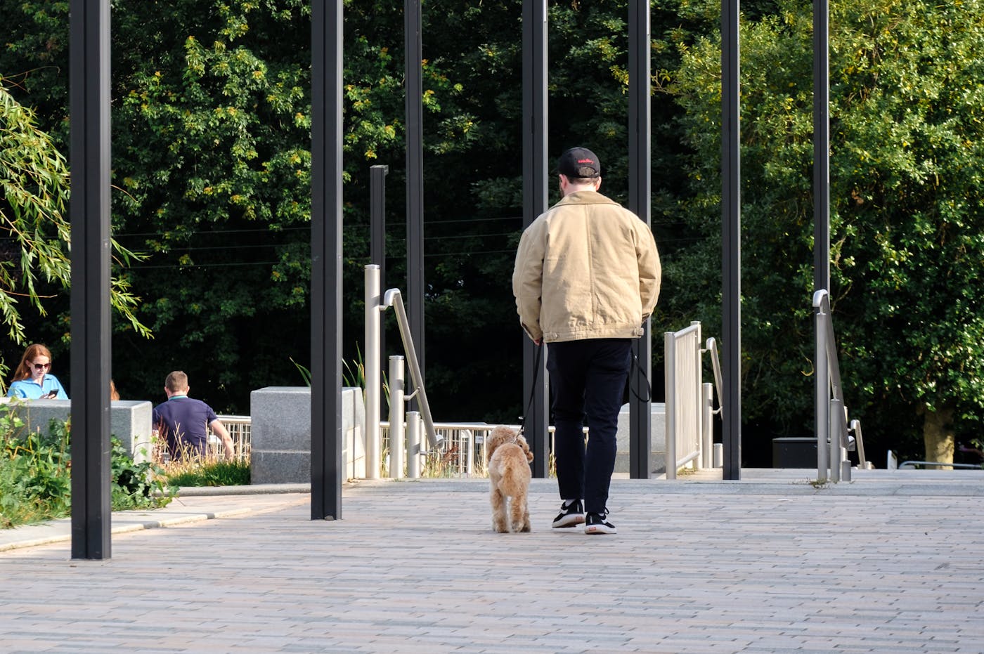 a man walking down a walkway with tall poles and a tower in the background