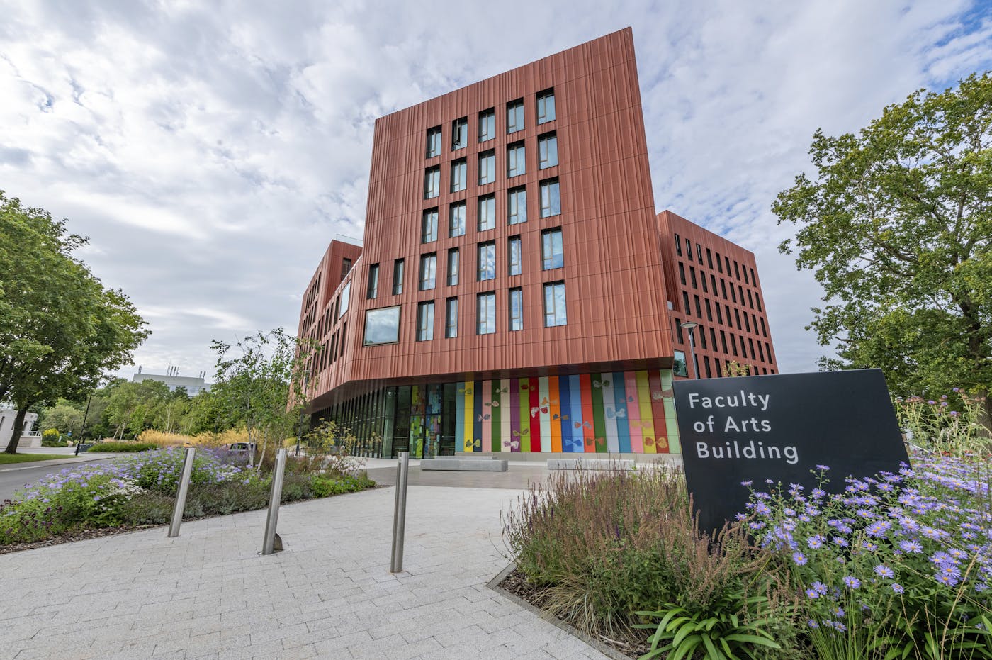 A large, modern building with a stone facade and a glass atrium. The building has a sign above the entrance that says "Faculty of Arts Building"