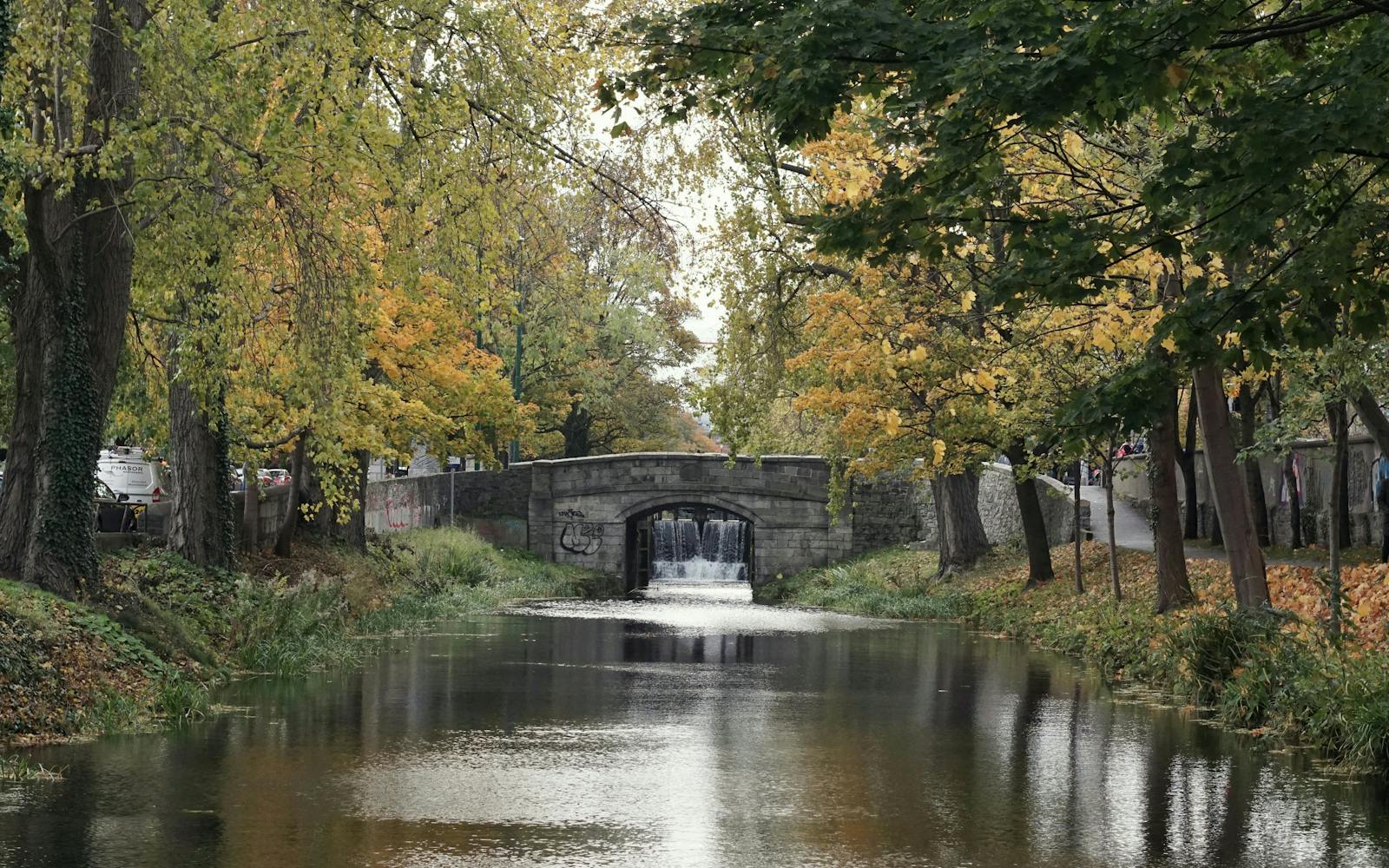 A scenic image of a stone arch bridge spanning a flowing river, surrounded by colorful trees in autumn