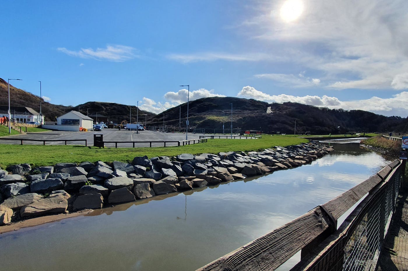 Waterway with stone wall in front of carpark with hills in the background