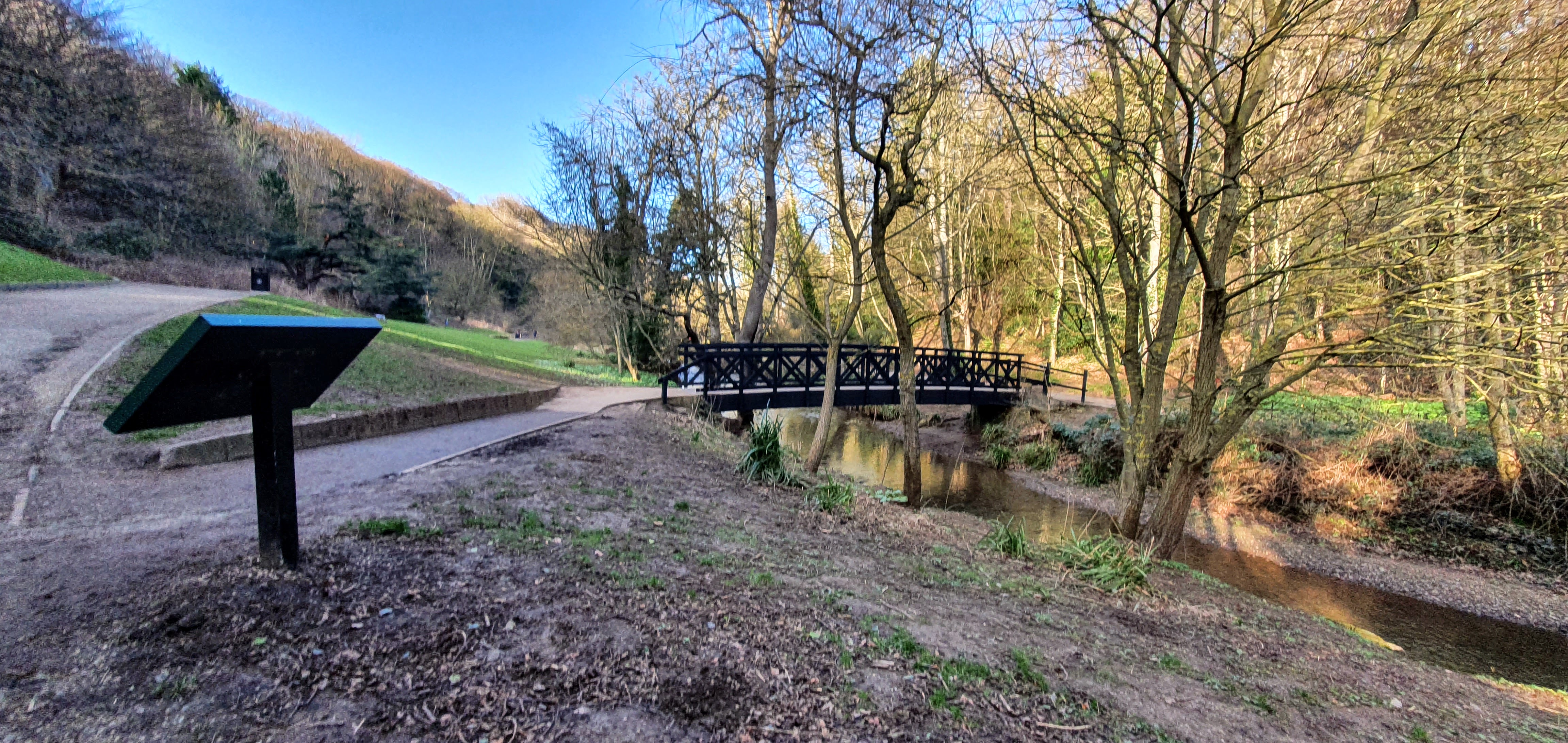 Path leading up to bridge over a stream through an area of woodland
