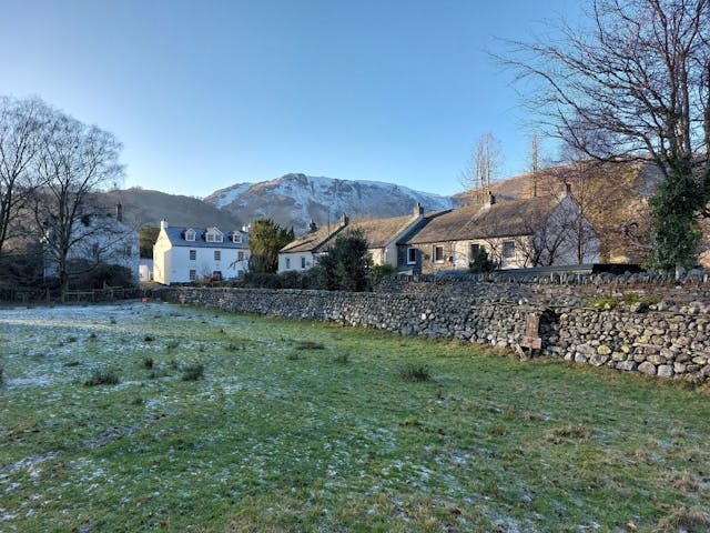Village comprising buildings positioned behind grass field and brick wall with snow topped mountains in the background