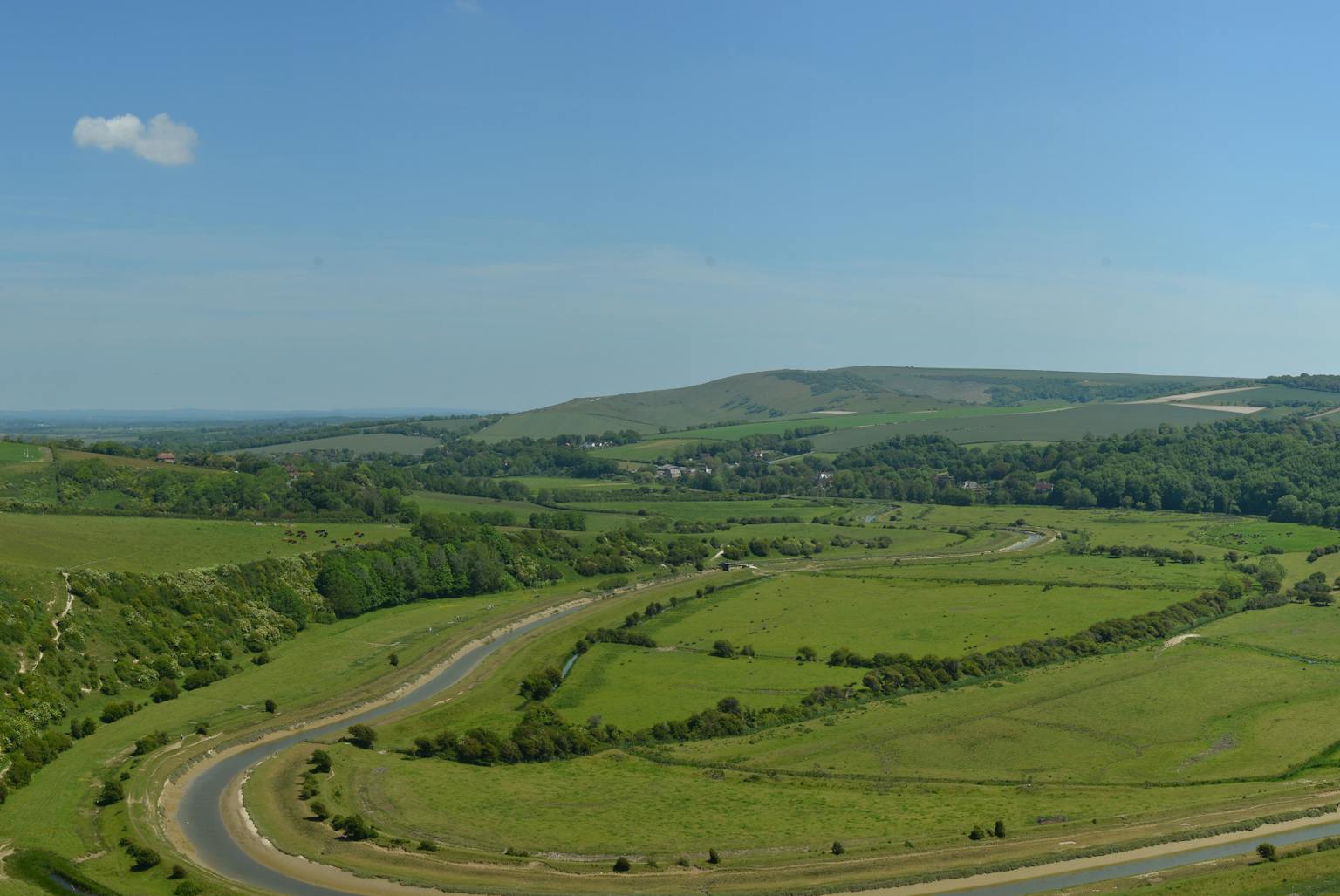 Aerial view of a meandering river flowing through a lush green valley with rolling hills in the background.