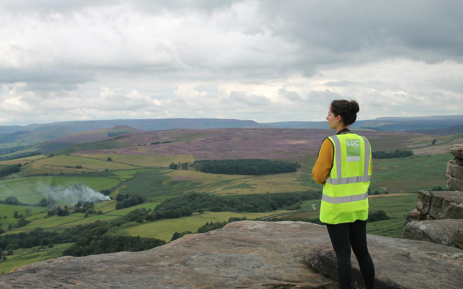 A person in a high-vis vest looking out over a Derbyshire landscape