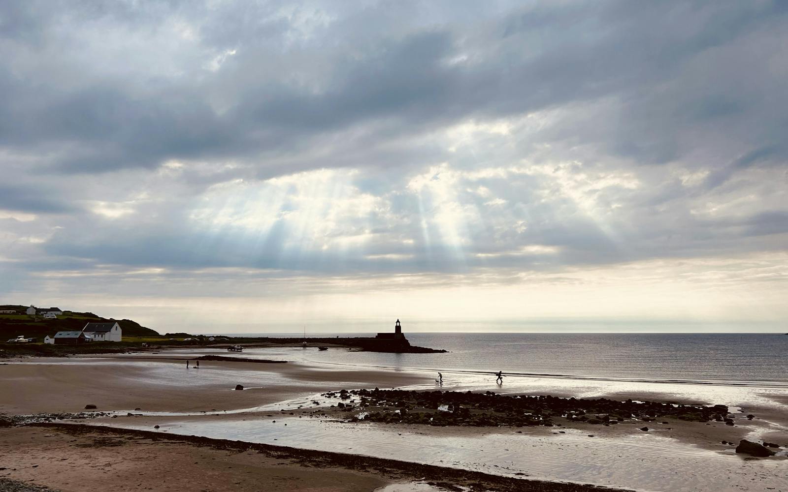 A beach with a lighthouse in the distance and sunrays peeking through the clouds
