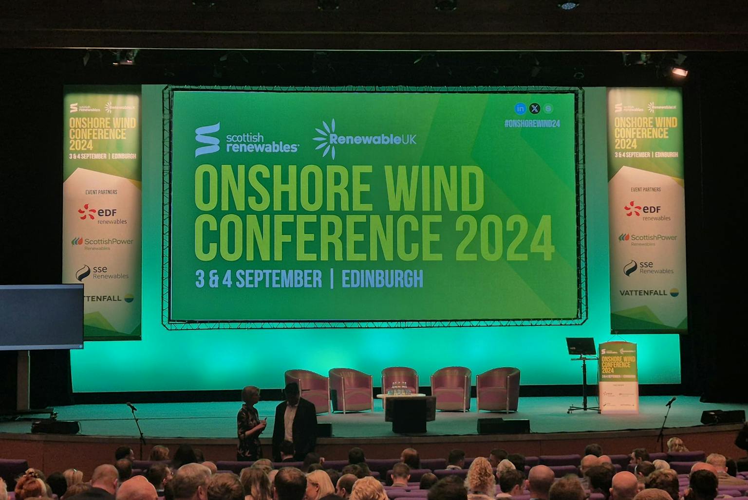Image of stage set up for panel discussion with big screen