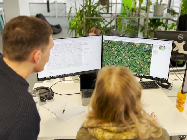 A person sat in front of a PC screen looking at a green aerial photo