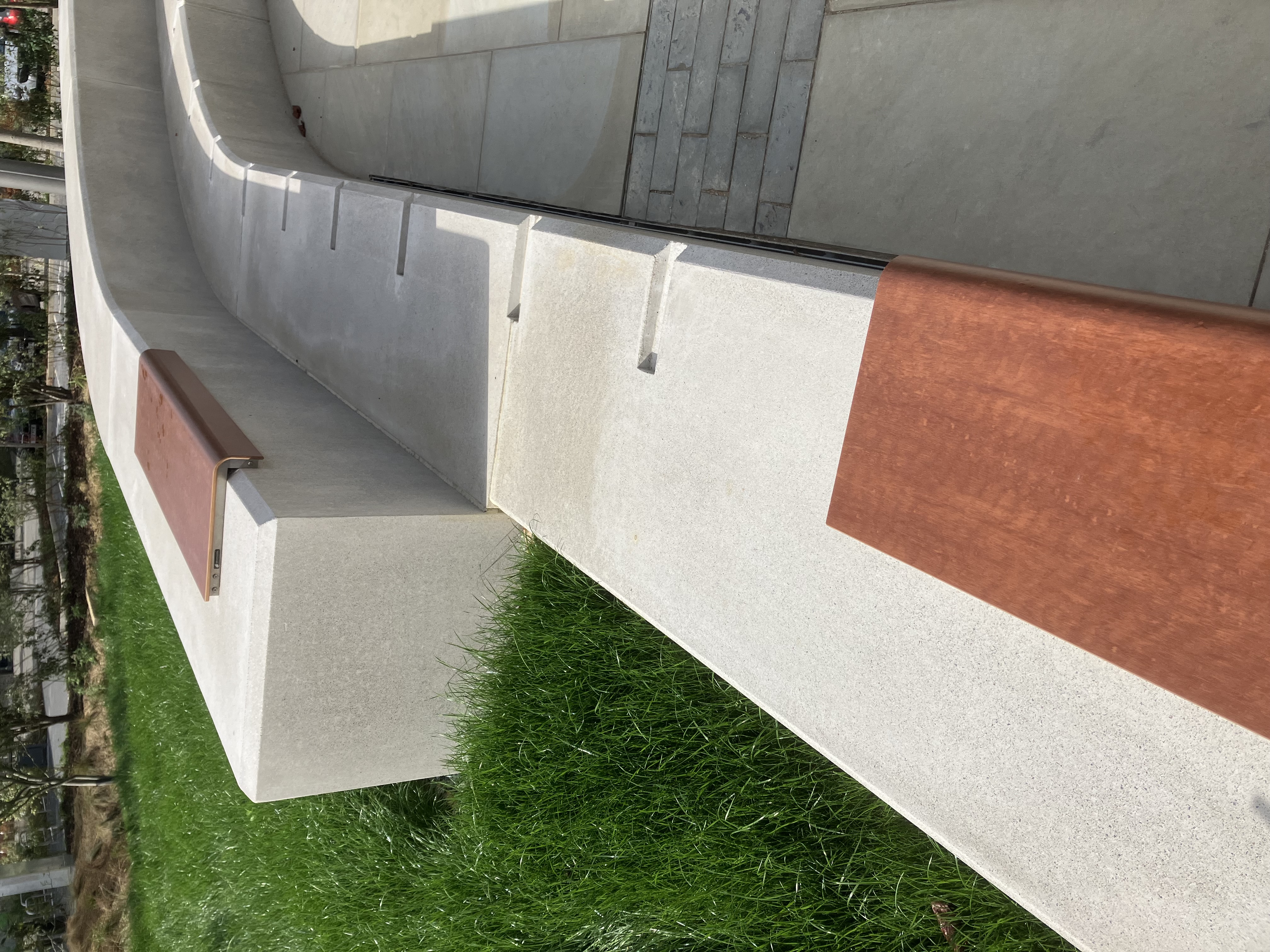 A curved concrete bench with wooden slats in a park setting.