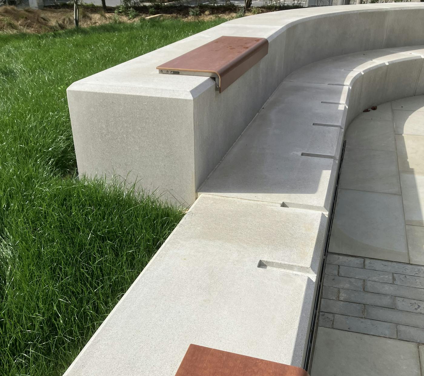 A curved concrete bench with wooden slats in a park setting.