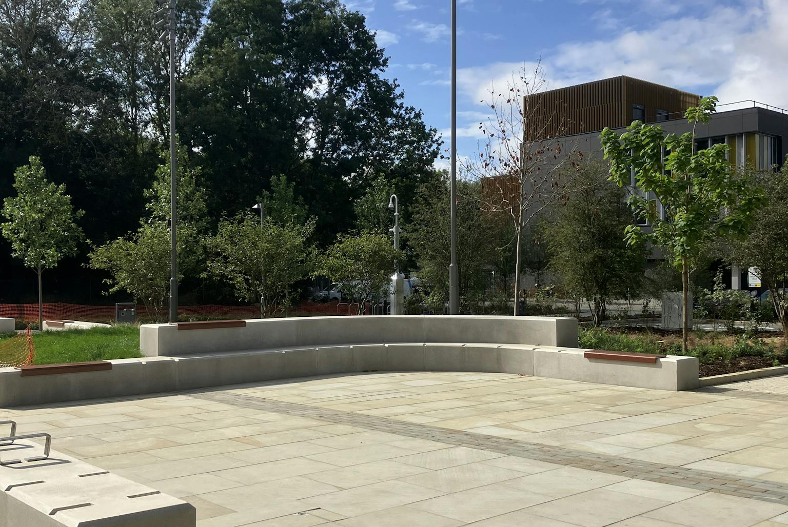 A paved outdoor seating area with benches, bordered by trees and landscaped greenery.