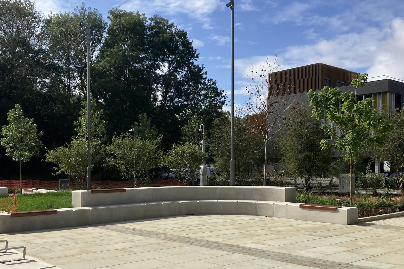A paved outdoor seating area with benches, bordered by trees and landscaped greenery.