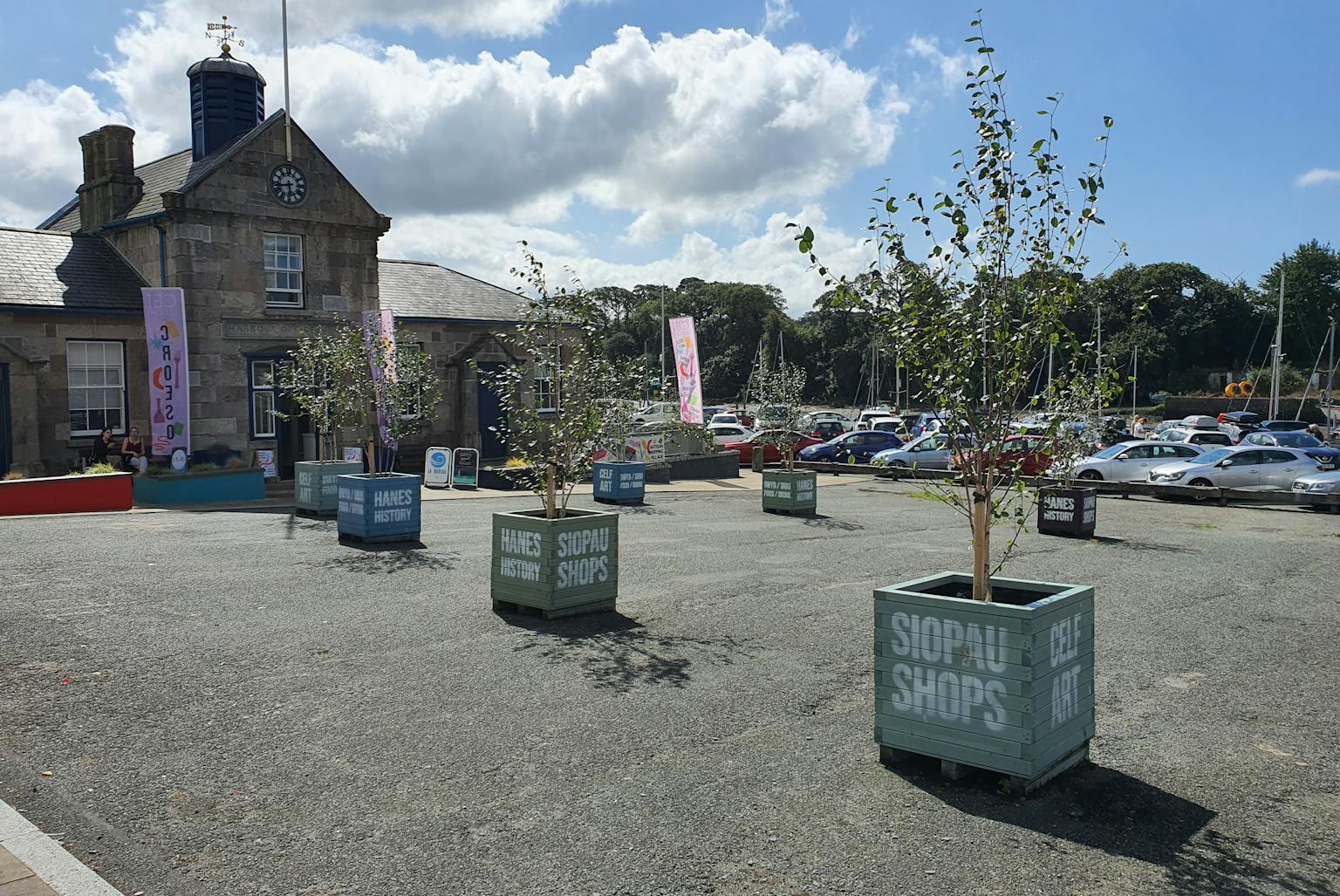 A paved square with planters and a building in the background. There are cars parked in the background.