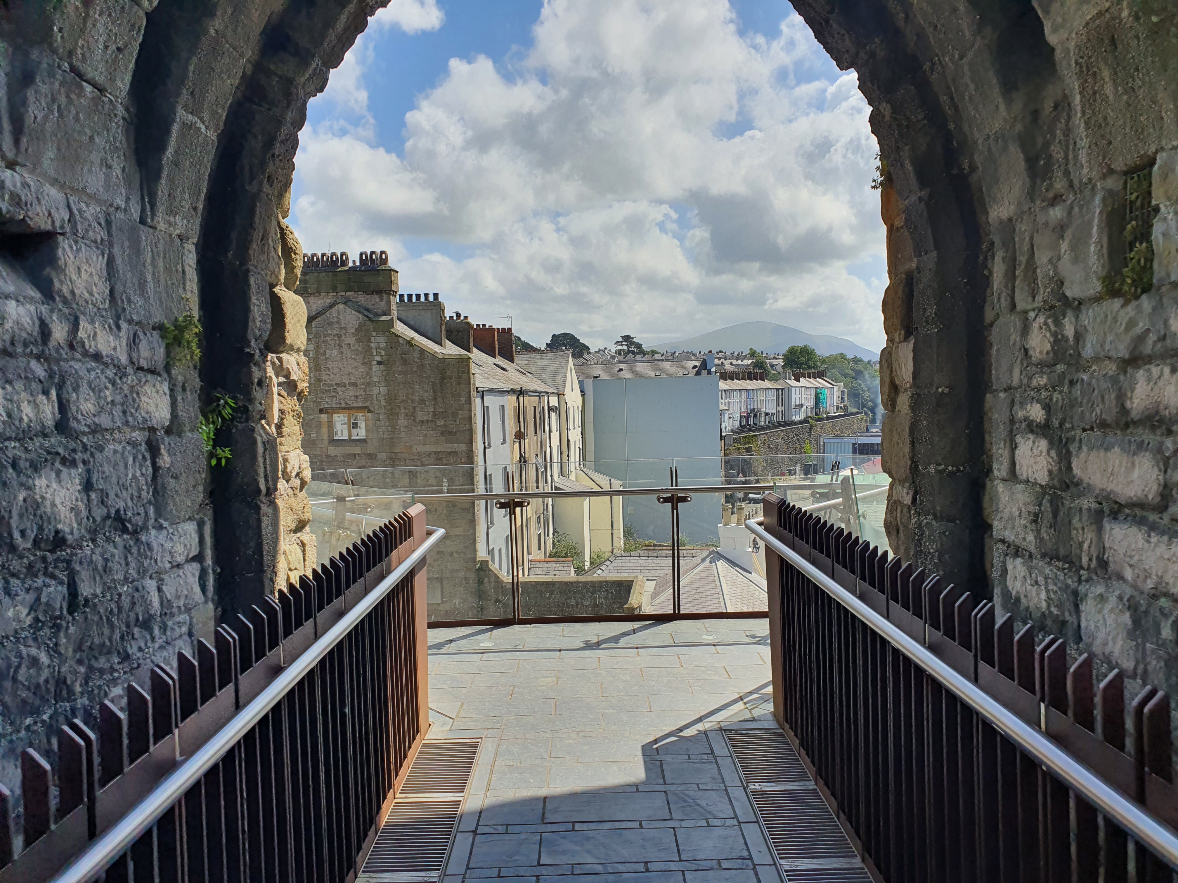 A stone archway leading to a walkway with a view of a town.
