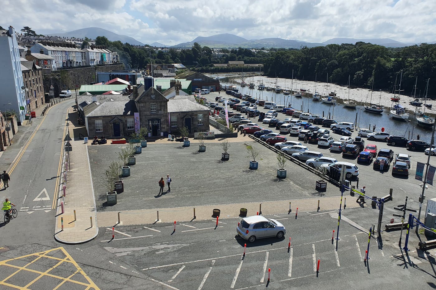 An aerial view of a coastal town with a harbor, a square, and a parking lot.