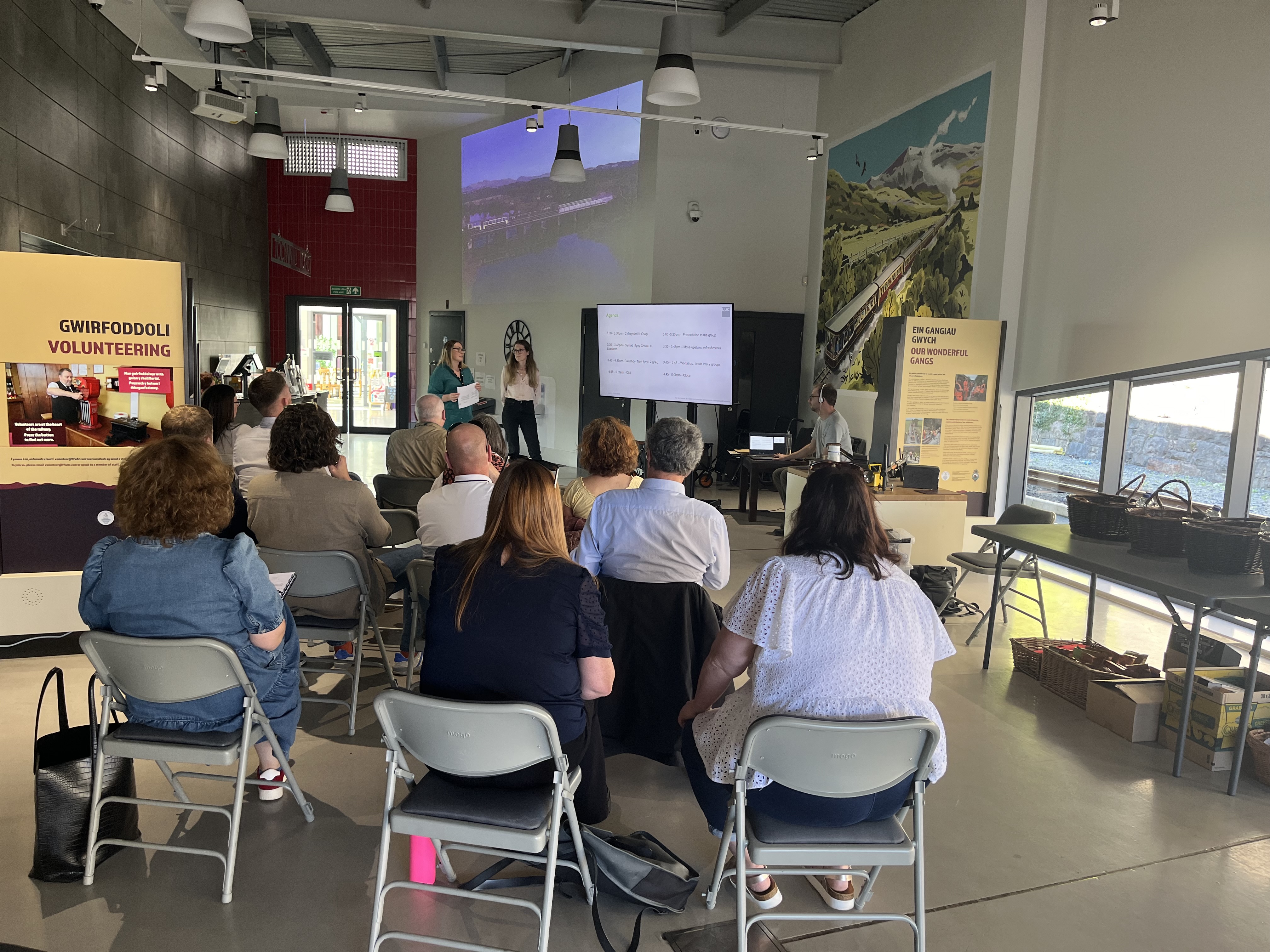 A group of people sat in a community hall listening to a presentation.