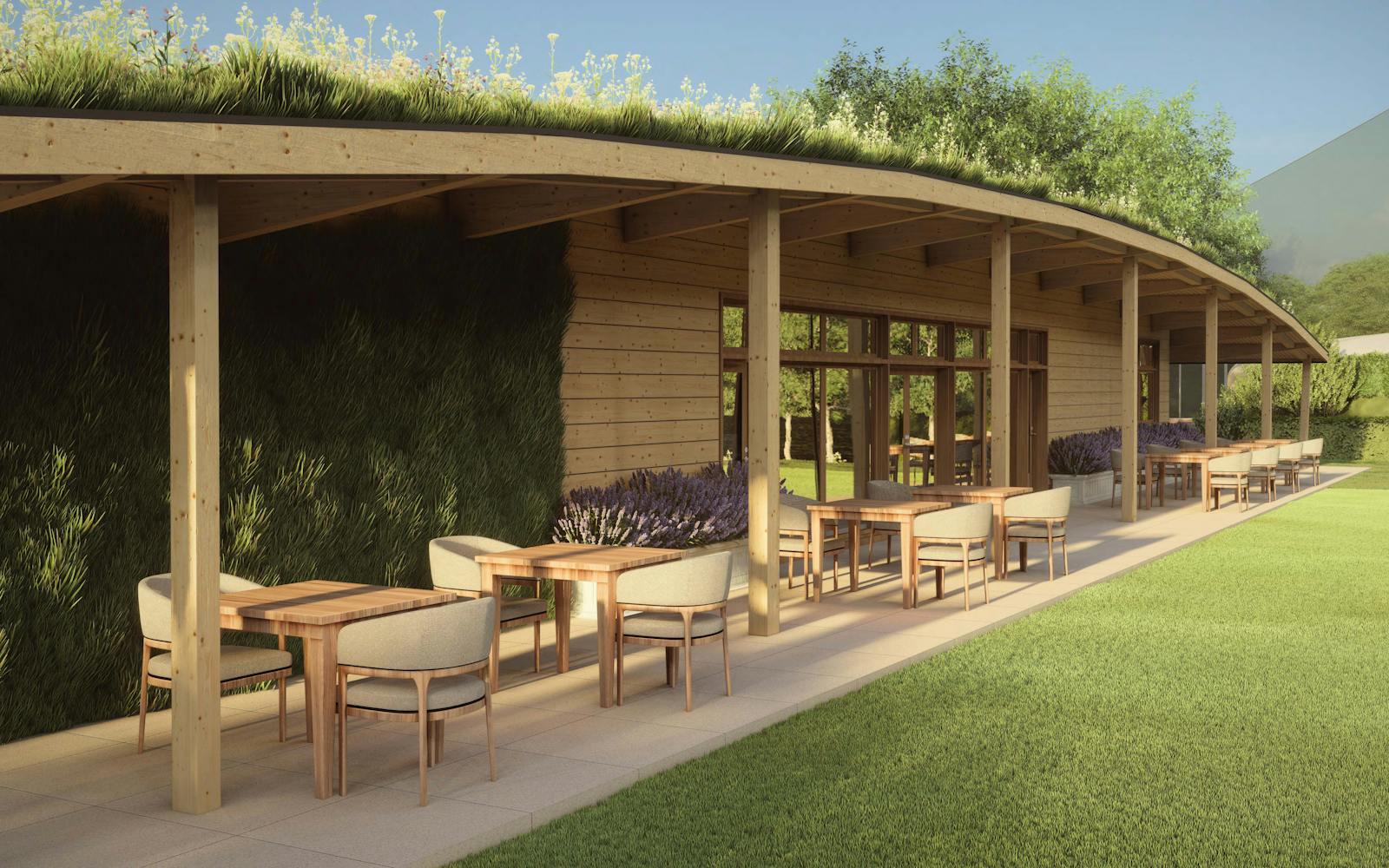 A modern, eco-friendly restaurant with a curved, green roof. Wooden pillars support a large overhang, providing shade for outdoor seating areas with tables and chairs. Lavender bushes line the base of the building, and lush greenery surrounds the restaurant.