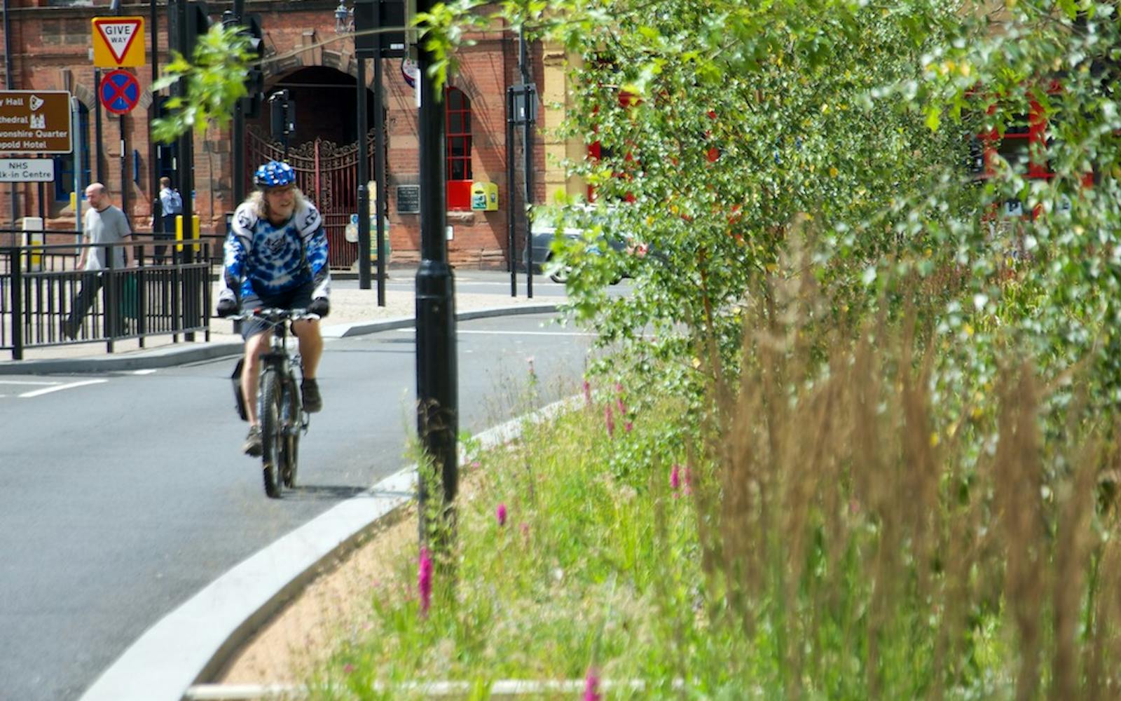 A person on a bike on a road riding past green trees and shrubs