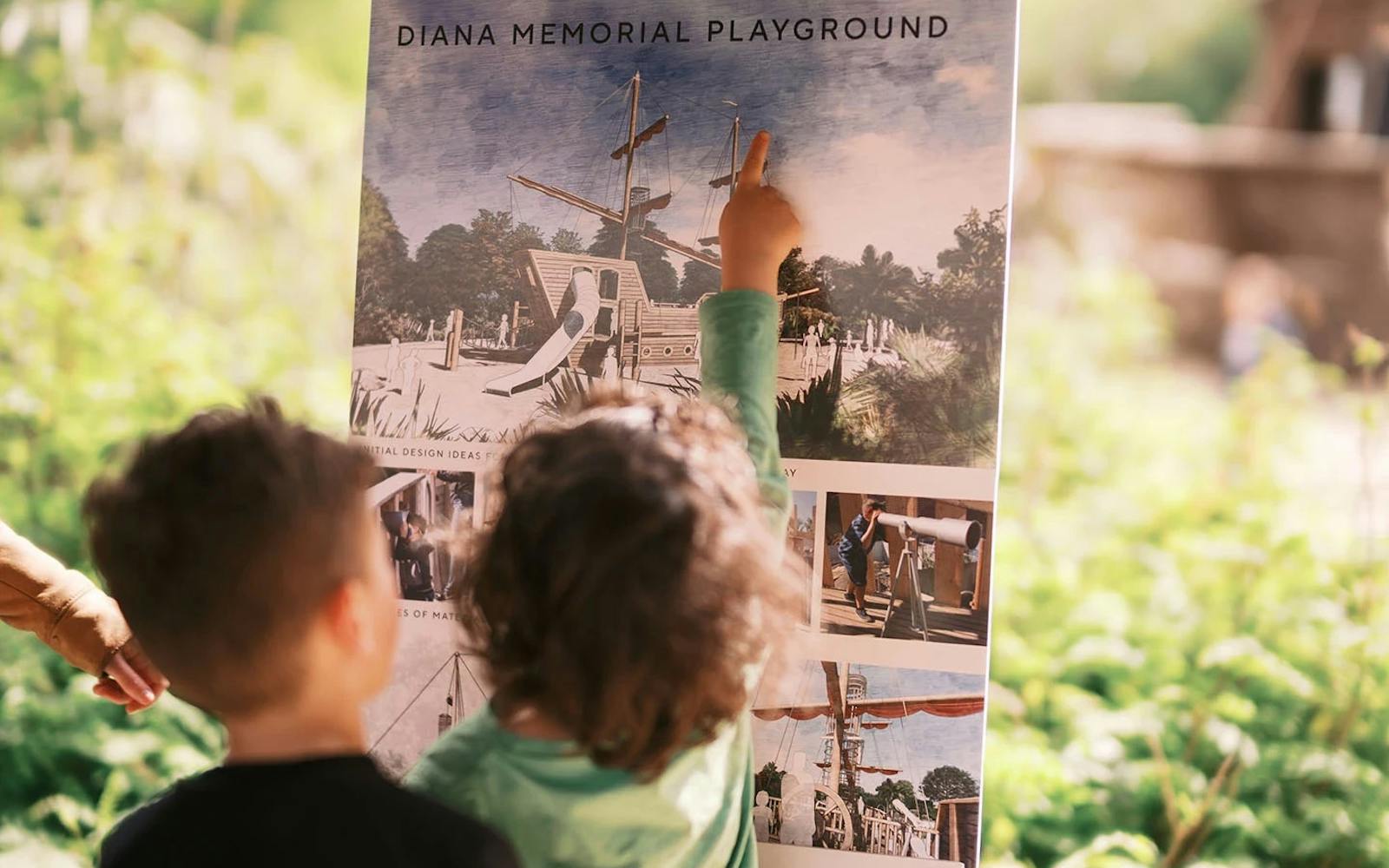 Two children look at a design board for the Diana Memorial Playground, with one child pointing at the pirate ship illustration.