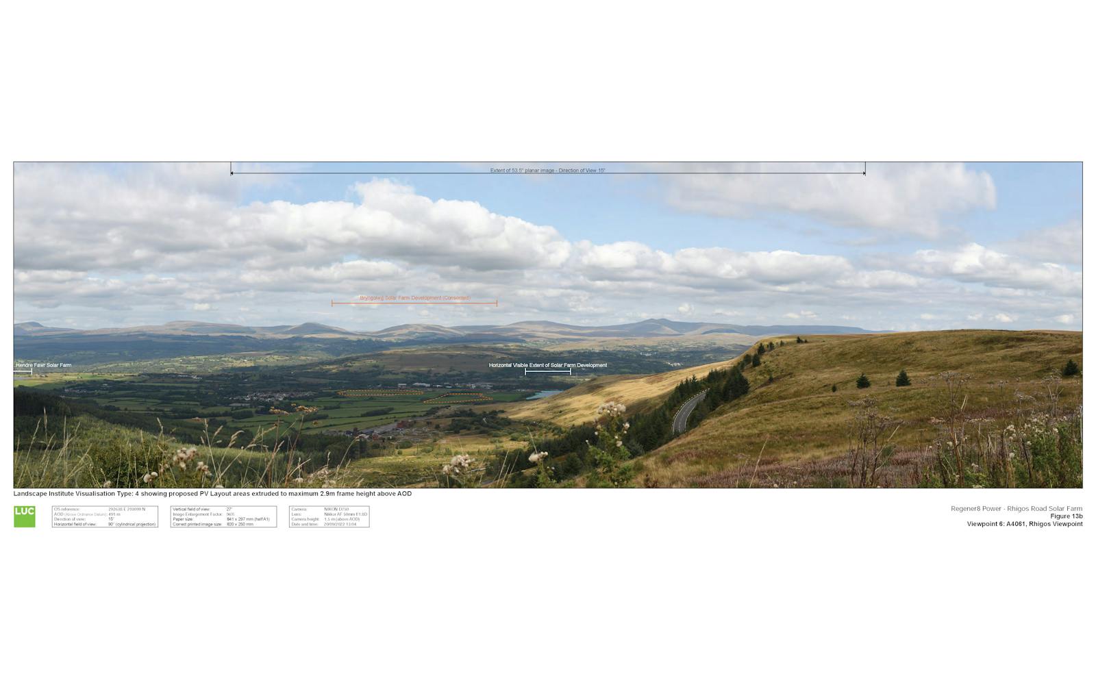A panoramic photograph taken from a hillside shows a valley with mountains in the distance under a cloudy sky.