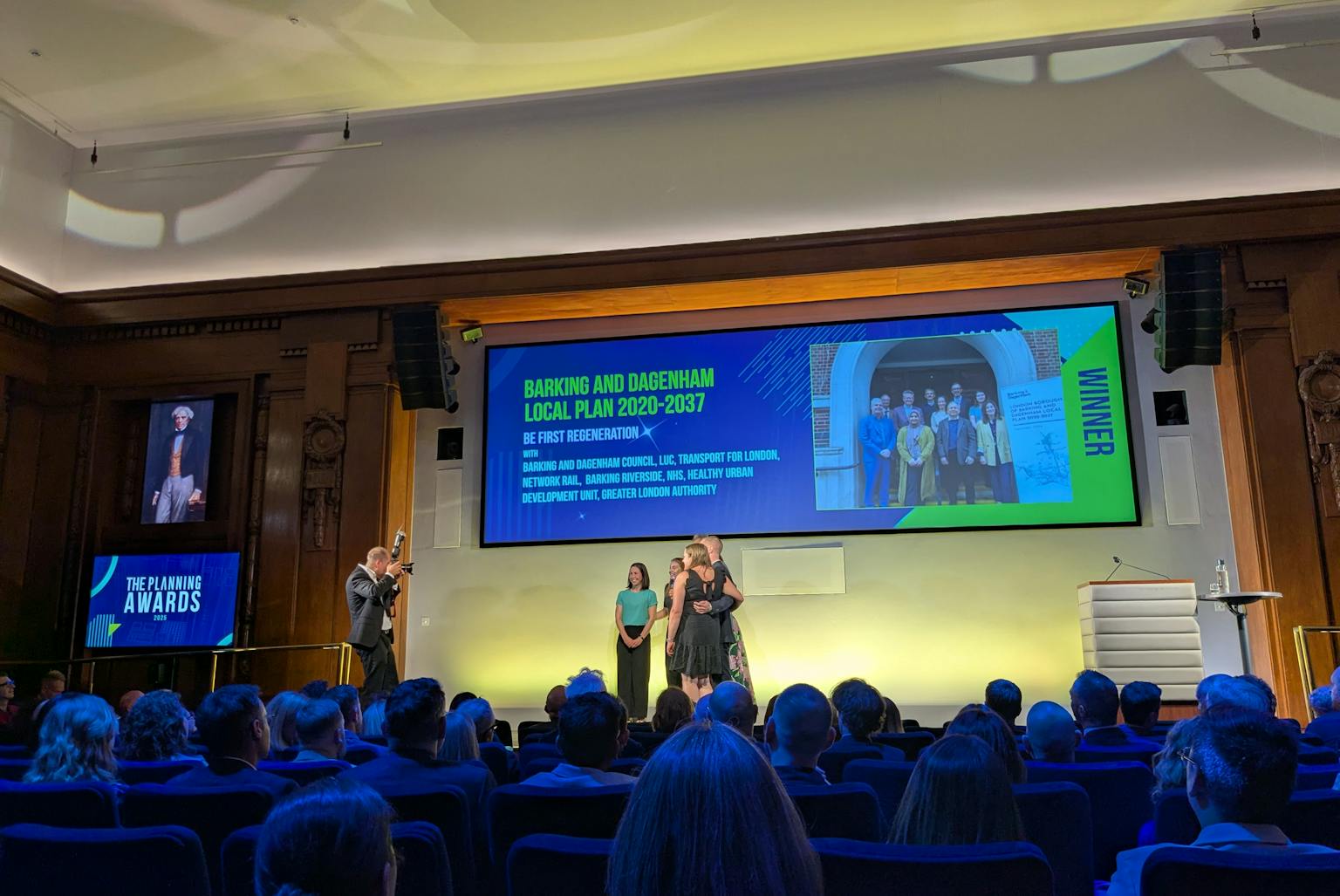 Some people on a stage underneath a large screen having their photo taken