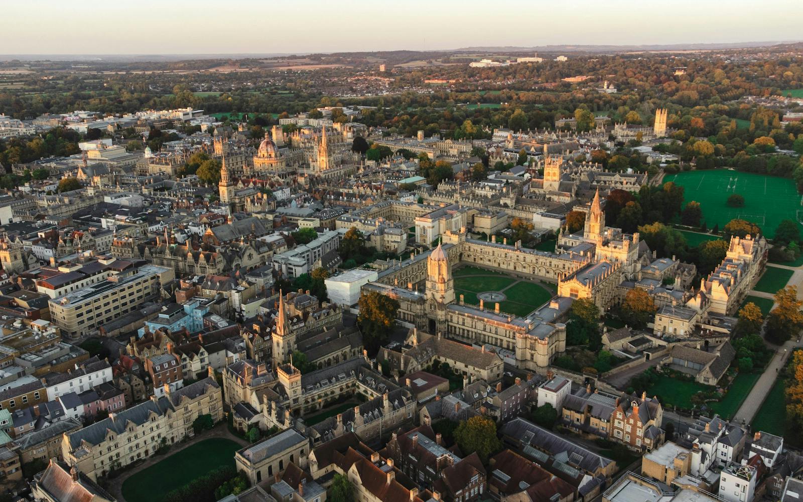 An aerial view of a historic city with numerous old buildings and green spaces, under a clear sky.