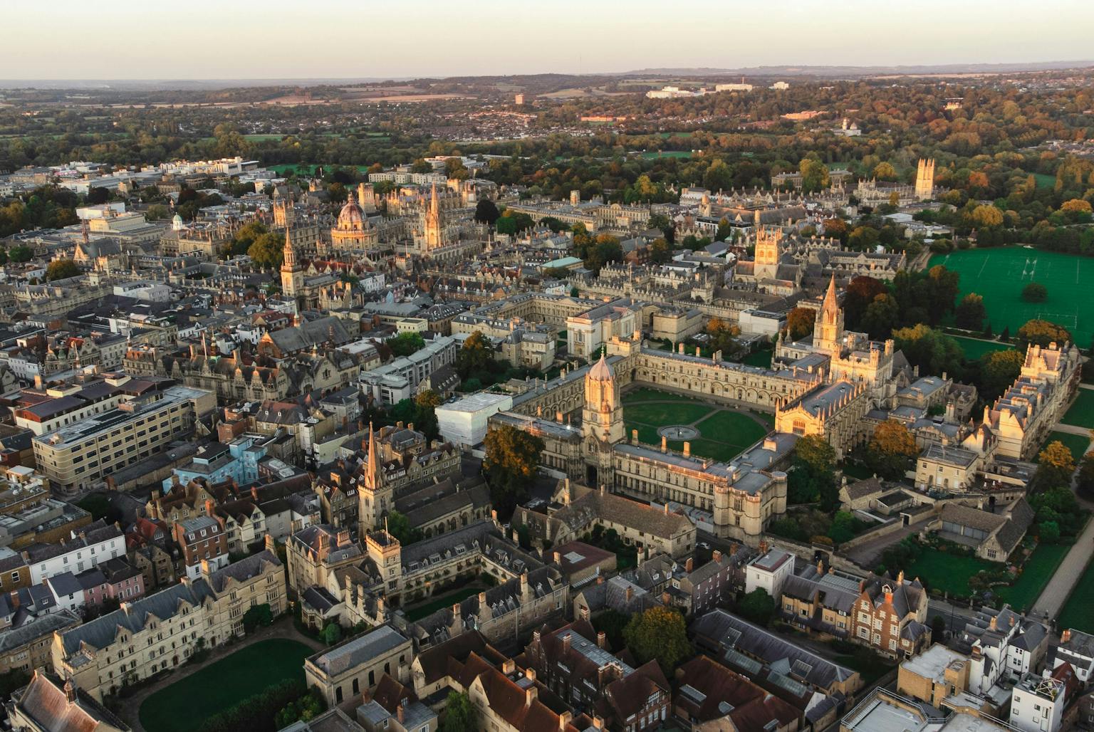 An aerial view of a historic city with numerous old buildings and green spaces, under a clear sky.