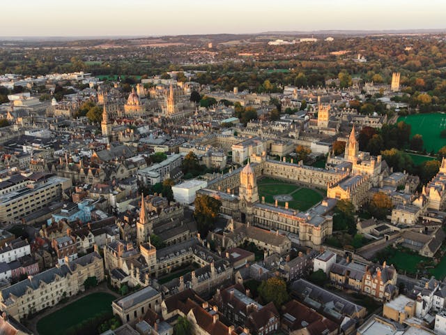 An aerial view of a historic city with numerous old buildings and green spaces, under a clear sky.