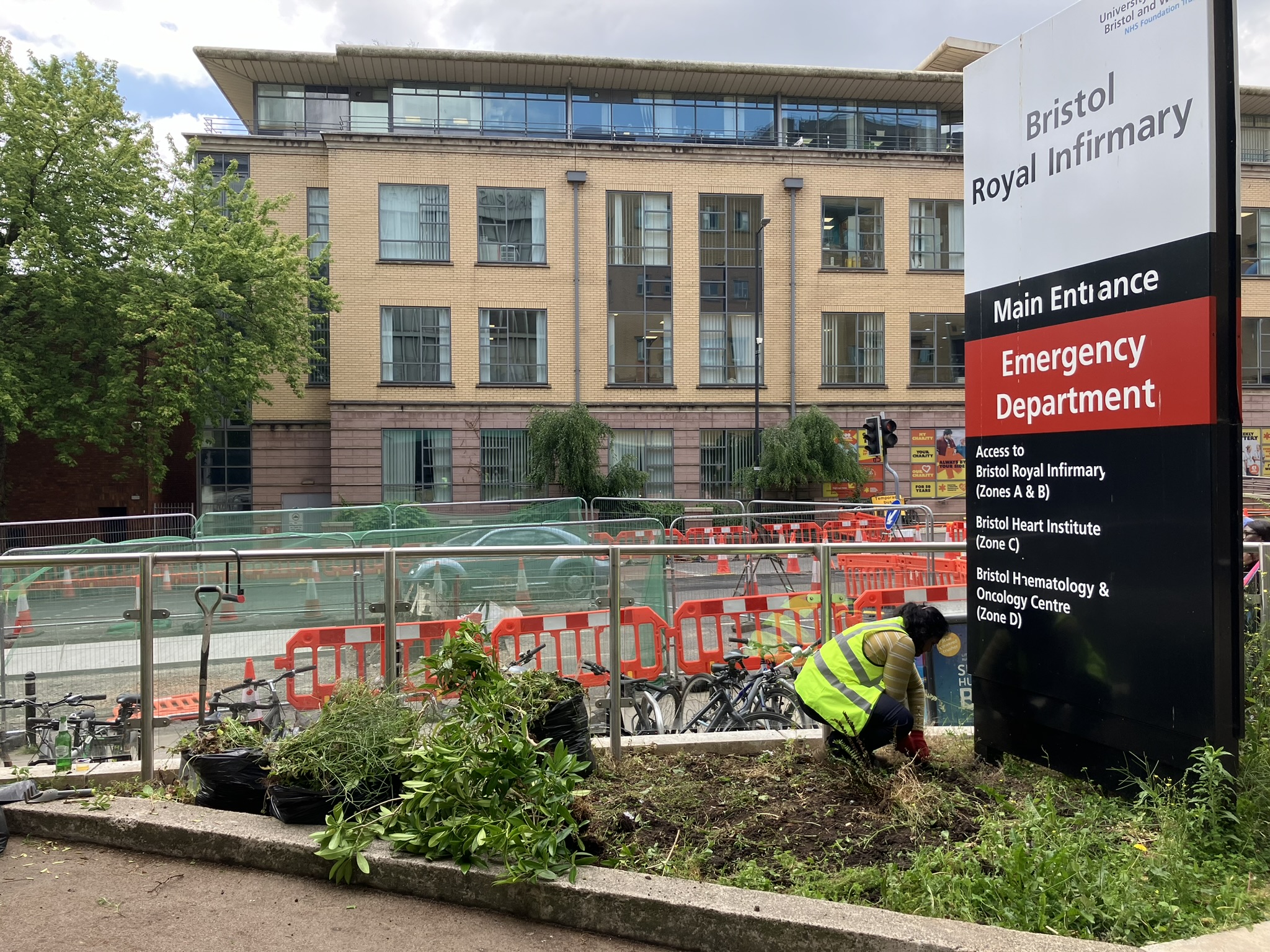 A person in high vis gardening a small patch of ground underneath a sign for Bristol Royal Infirmary